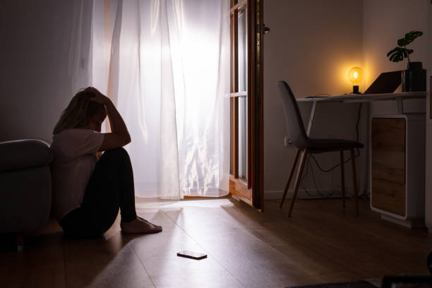 Sad depressed woman crying at home. Dark room. Side view full length shot of a sad depressed woman sitting on the floor and crying at home mental health awareness stock pictures, royalty-free photos & images