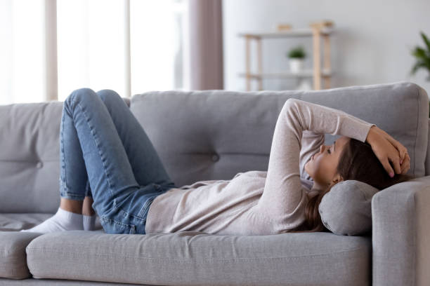 Sad depressed young woman lying on couch feeling headache Sad depressed young woman lying on couch at home feeling headache fatigue loneliness, upset tired sick ill teen girl suffer from migraine anxiety, drowsy somnolent teenager rest on sofa after stress chronic illness stock pictures, royalty-free photos & images