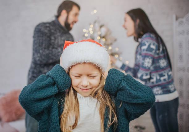 Sad, desperate little girl during parents quarrel. Clog the ears.. Family quarrel on the eve of Christmas. stock photo