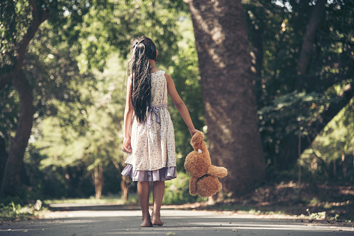 Sad girl hugging teddy bear sadness alone in green garden park. Lonely girl feeling sad unhappy walking outdoors with best friend toy. Autism child play teddy bear best friend. Family violence concept