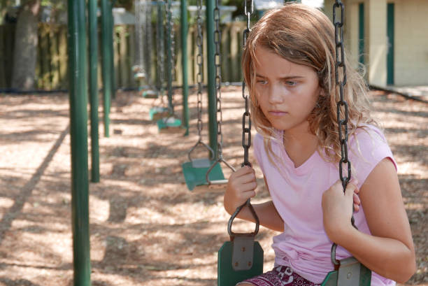 Sad girl sitting alone on a swing in a playground stock photo