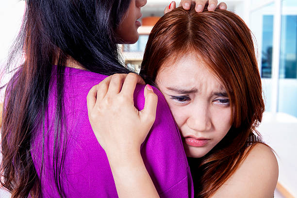 Sad girl soothed by her friend Depressed teenage girl soothed by her friend while embrace each other at home two asian woman hugging and crying stock pictures, royalty-free photos & images