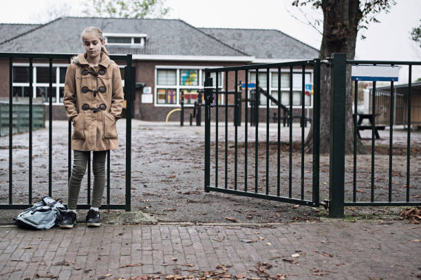 Sad girl standing at school entrance alone stock photo