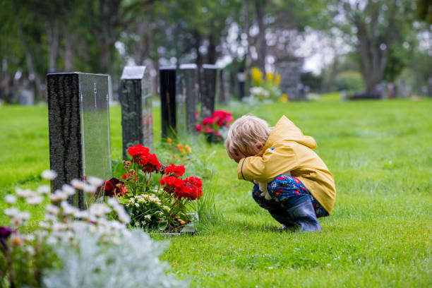 Sad little child, blond boy, standing in the rain on cemetery, sad person, mourning stock photo