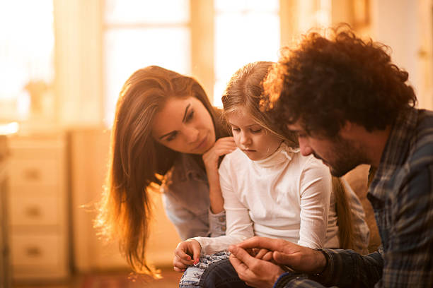Sad little girl at home being consoled by her parents. Young parents spending time with their small daughter and consoling her. displeased photos stock pictures, royalty-free photos & images