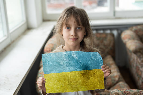 Sad little girl covered with Ukraine flag stock photo