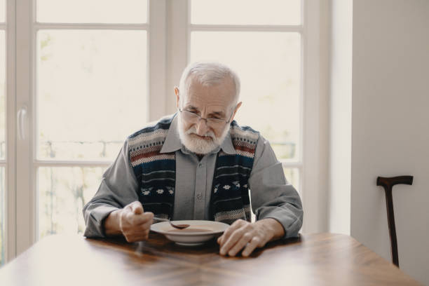 trauriger einsamer senior essen suppe in leerer wohnung - einsamkeit stock-fotos und bilder