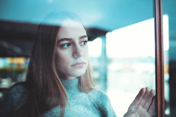 sad lonely young woman looking thoughtfully through window stock photo