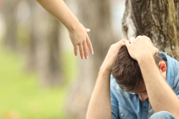 Sad teen and a hand offering help Sad teen sitting on the grass in a park and a woman hand offering help with a green background forgiveness stock pictures, royalty-free photos & images