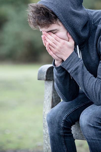 sad teenage boy sitting on a bench - alleen één tienerjongen stockfoto's en -beelden