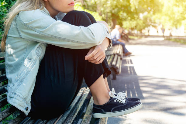 Sad teenage girl sitting on the park bench stock photo