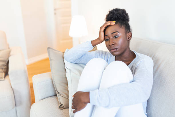 Sad thoughtful worried african american girl sit on sofa looking away feel depressed doubtful, lonely stressed upset young black girl thinking of psychological problem thinking regret about mistake stock photo