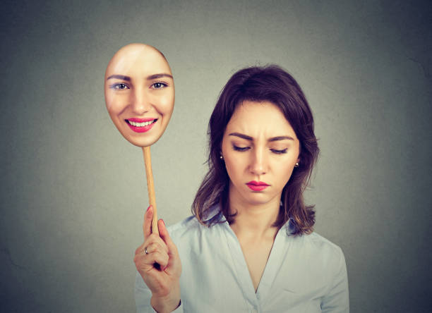 Sad woman looking down taking off happy mask of herself stock photo