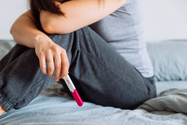 sad woman on bed with negative pregnancy test stock photo