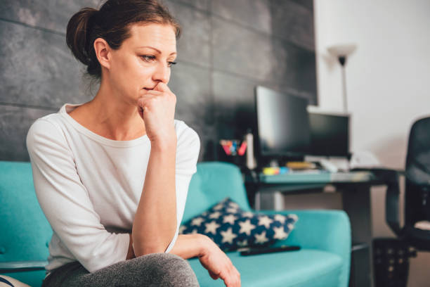 Sad woman Sad woman sitting on a sofa in the living room anxiety stock pictures, royalty-free photos & images