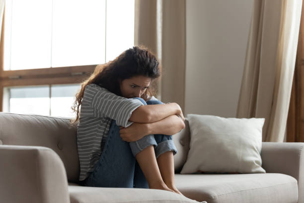 Sad woman sitting on couch feels lonely goes through divorce Sad woman hug knees sit on couch feels lonely goes through divorce or break up. Female with drug or alcohol addiction problem need rehab help. Unplanned pregnancy made decision about abortion concept anxiety stock pictures, royalty-free photos & images