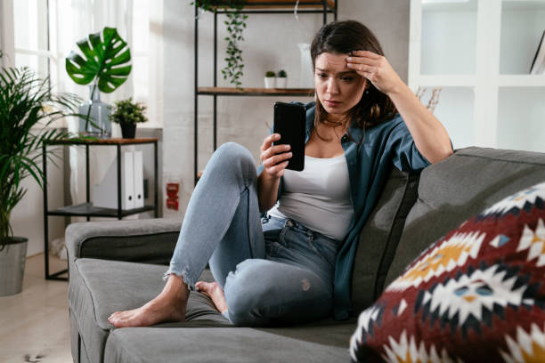 Sad woman sitting on the couch, using the phone stock photo