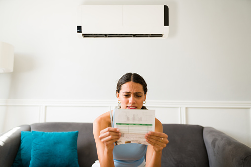 Worried young woman looking stressed while receiving the electricity bill after using the air conditioner at home