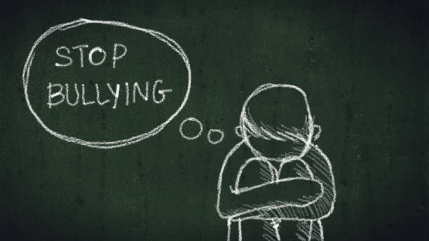 sad young boy sitting on the floor with text stop bullying written with chalk on chalkboard. social problems of humanity stock photo