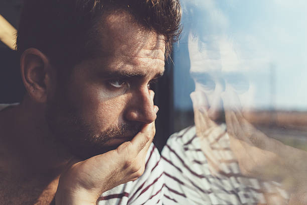Sad young man looking through the window Sad young man looking through the window grief photos stock pictures, royalty-free photos & images