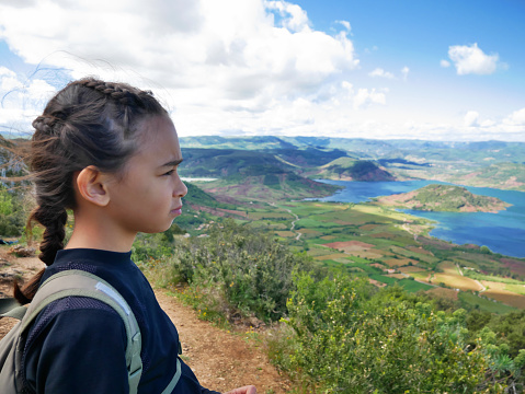 A sad young multiracial female hiker with a backpack looking at Salagou lake in France