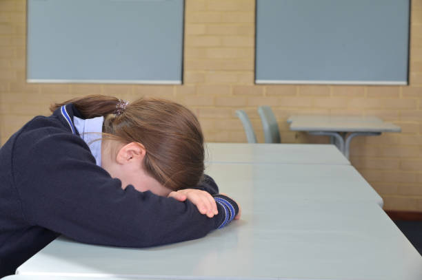 Sad young schoolgirl  sitting in classroom alone after being bullied stock photo
