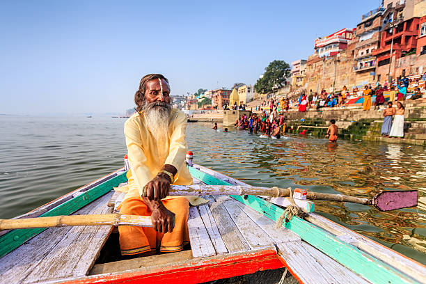 Sadhu rowing boat on the holy Ganges River in Varanasi In Hinduism, sadhu, or shadhu is a common term for a mystic, an ascetic, practitioner of yoga (yogi) and/or wandering monks. The sadhu is solely dedicated to achieving the fourth and final Hindu goal of life, moksha (liberation), through meditation and contemplation of Brahman. Sadhus often wear ochre-colored clothing, symbolizing renunciation. ganges river stock pictures, royalty-free photos & images