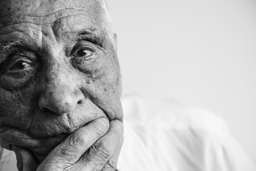 An old man looking at camera, covering his mouth with his hand. Black and white photo.