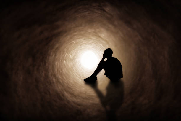 Sadness The silhouette of a teenage boy upset and covering his face as he sits in a dark tunnel. depression land feature stock pictures, royalty-free photos & images