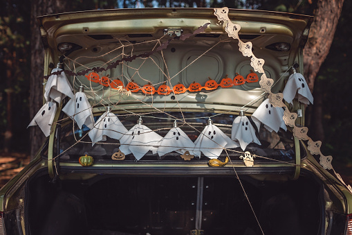 Alternative safe celebration. Cute kids preparing Halloween party in the trunk of car with carved pumpkin, spider net, ghosts and other decoration for Halloween, autumn outdoor.