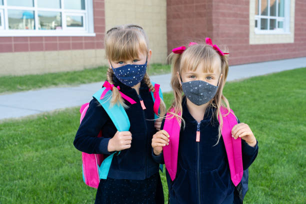 Safety back to school concept, wearing mask and using hand sanitizer for students. Two young sisters going to school stock photo