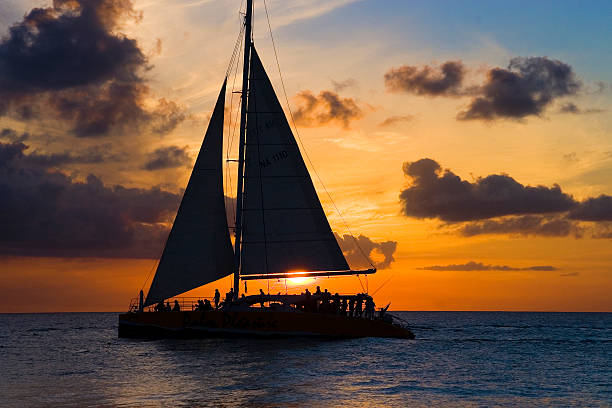Sailboat and sunset Beautiful sailboat back lit by a stunning sunset, Eagle Beach, Aruba. catamaran stock pictures, royalty-free photos & images