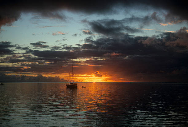 Sailboat at sunset, South Pacific A lone sailboat with brooding clouds and a tiny hint of the last piece of the sun as it is going down. hearkencreative stock pictures, royalty-free photos & images