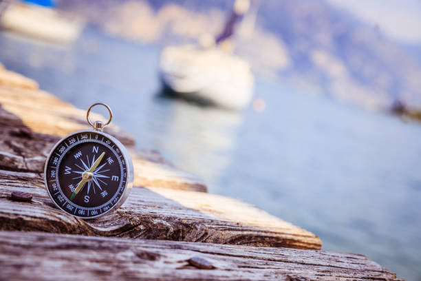 Sailing: nautical compass on wooden dock pier. Sailing boats in the background. stock photo