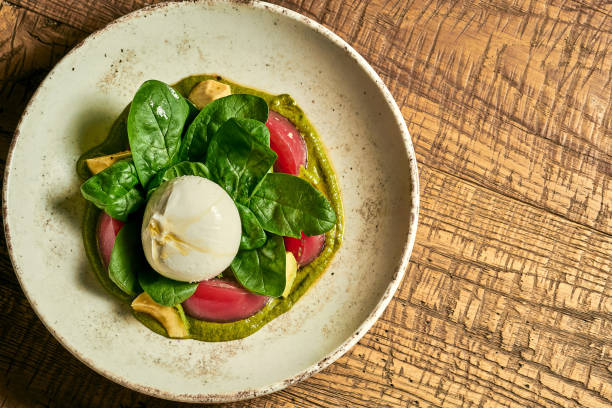 Salad with burrata, tomatoes, basil and pesto in a plate on a wooden background stock photo