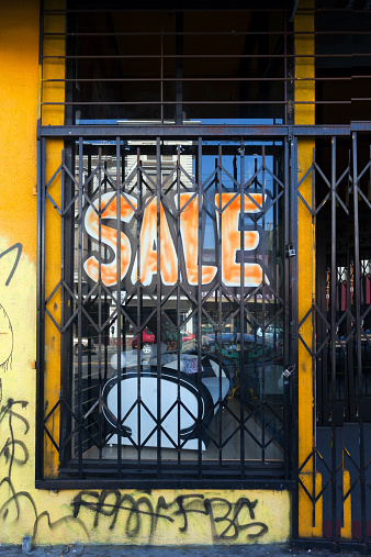 Store SALE sign behind window security bars and graffiti walls. Vertical.
