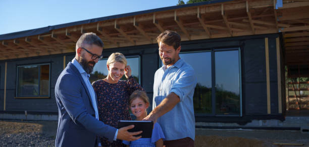 Sales Agent showing plans of new house to young family on construction site. stock photo