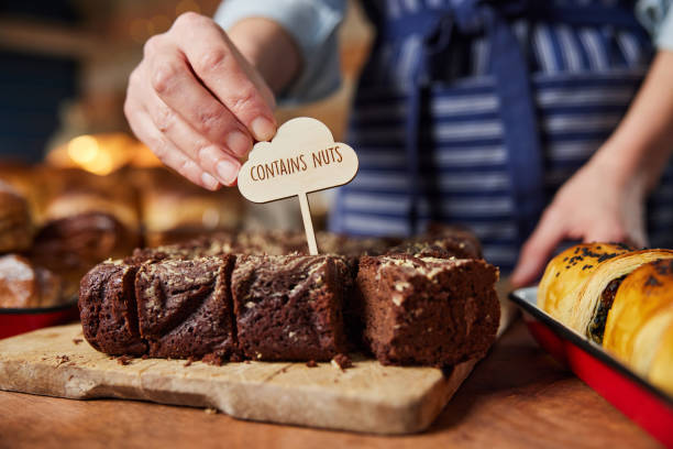 Sales Assistant In Bakery Putting Contains Nuts Label Into Stack Of Freshly Baked Baked Brownies stock photo