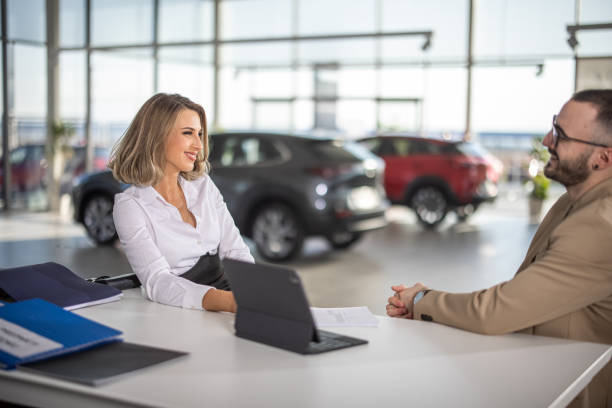 Sales woman sitting and talking with male customer in car dealership stock photo