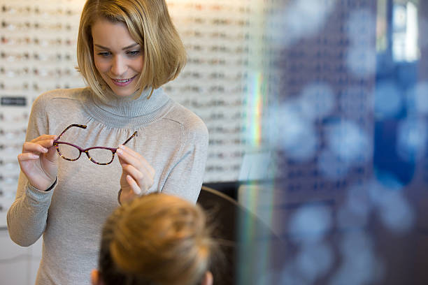 Salesgirl Assisting Customer To In Wearing Glasses Salesgirl Assisting Customer To In Wearing Glasses salesgirl stock pictures, royalty-free photos & images