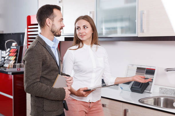 Salesgirl consulting male customer in store of kitchen furnishing Positive salesgirl consulting male customer in store of kitchen furnishing and appliances salesgirl stock pictures, royalty-free photos & images