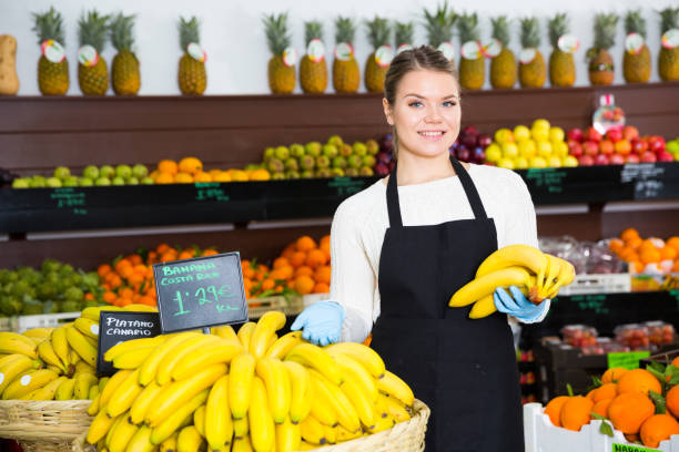 Salesgirl proposing bananas Portrait of young smiling saleswoman with yellow bananas in store salesgirl stock pictures, royalty-free photos & images