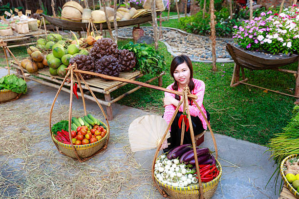 salesgirl with her bamboo basket full of vegetables Hochiminh City, Vietnam - March 5, 2016 : salesgirl with her bamboo basket full of vegetables in the culinary fair at the Van Thanh tourist area, Ho Chi Minh City which is modeled on the traditional market in the village Vietnam salesgirl stock pictures, royalty-free photos & images