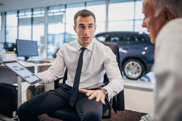 Salesman talking to a senior male customer at the car dealership store Two people, young salesman talking with senior male buyer at the car dealership store. car salesperson stock pictures, royalty-free photos & images