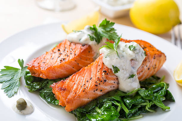 Salmon Steak with Cream Sauce Grilled Salmon on a Bed of Spinach, Cream Sauce and Lemon Wedges caper stock pictures, royalty-free photos & images