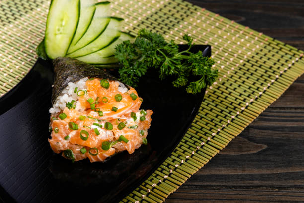 Salmon temaki sushi on black plate in black background. Japanese cuisine stock photo