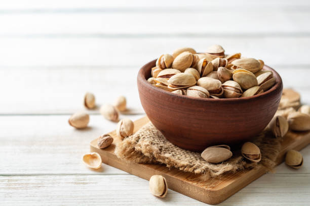 Salted pistachio nuts in ceramic bowl on white wooden background stock photo