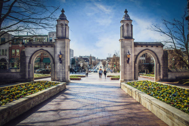 Sample Gates leading out of Indiana University into downtown with students and a senior lady walking and running and many cars in early spring stock photo