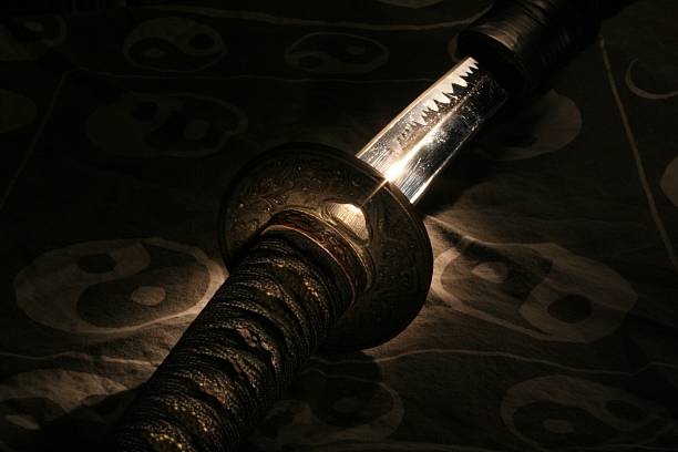 Samurai sword on a yin yang background A selectively lit samurai sword on a cloth with yin-yang symbols. Light is reflecting off of the blade. bushido lifestyle stock pictures, royalty-free photos & images