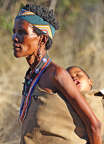 San bush woman with child in papoose on back, Makgadikgadi Pans, Botswana, Southern Africa. The San are an ancient indigenous tribal people who inhabited much of southern Africa and although few in number today remain proud of their culture, ancestry and traditional ways of dress, customs and behaviour that included subsistence hunting and foraging
